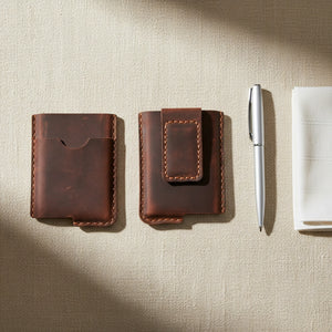 Two brown leather card holders, one with a money clip, styled with a pen on linen