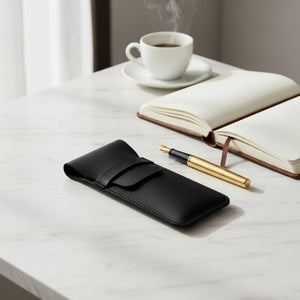 Black leather pen case with a gold fountain pen, notebook and coffee on marble