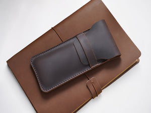 Coffee brown leather pen case resting on a leather journal