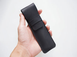 Hand holding a slim black leather pen case for scale