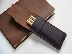 Coffee brown leather pen case holding gold pens on a journal