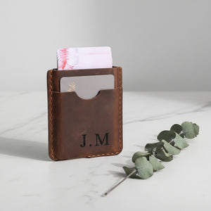 Engraved J.M brown leather card holder with cards popping up, on marble