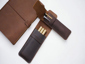 Open coffee brown leather pen case revealing gold pens