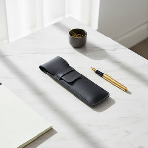 Black leather pen case with a gold fountain pen on a marble desk