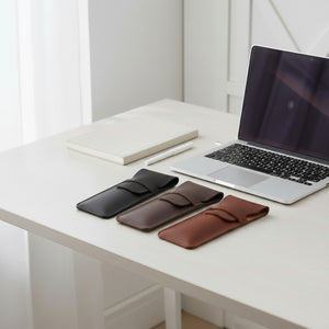 Three leather pen cases in black, coffee and brown on a desk with a laptop