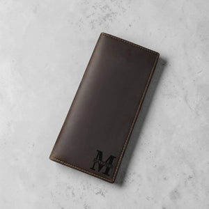 Hand holding open engraved leather long wallet showing inside personalization on a wood desk